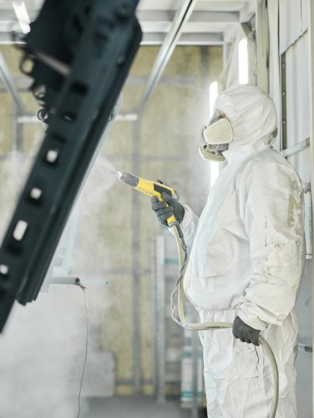 Man with spray gun painting metal in factory